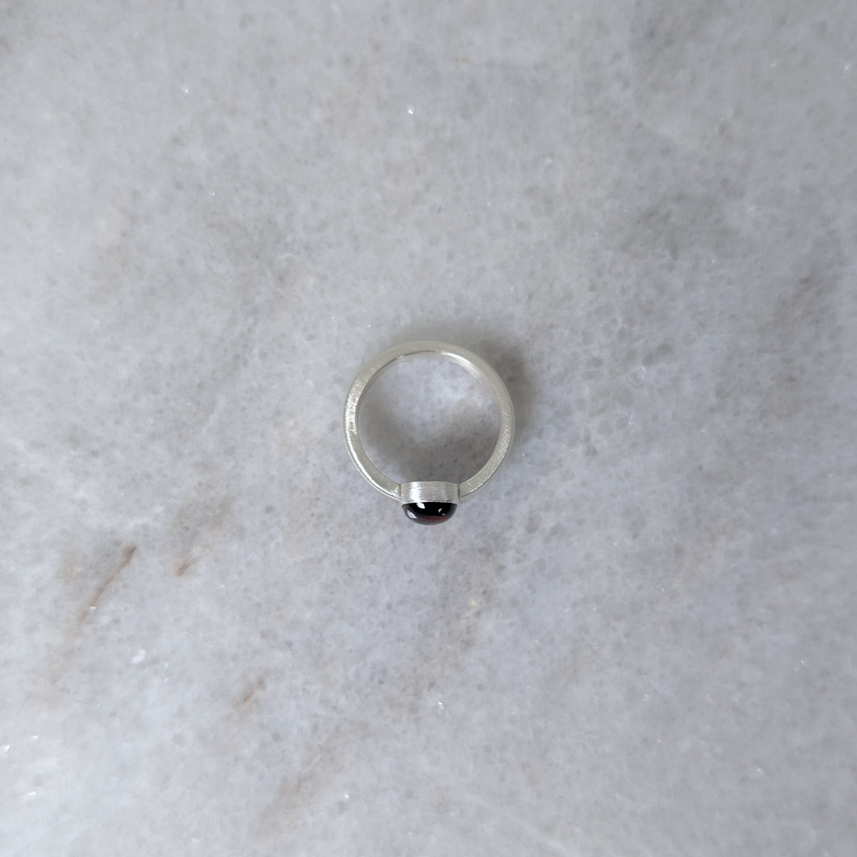 Side view of silver ring with a garnet center stone on a white marble surface