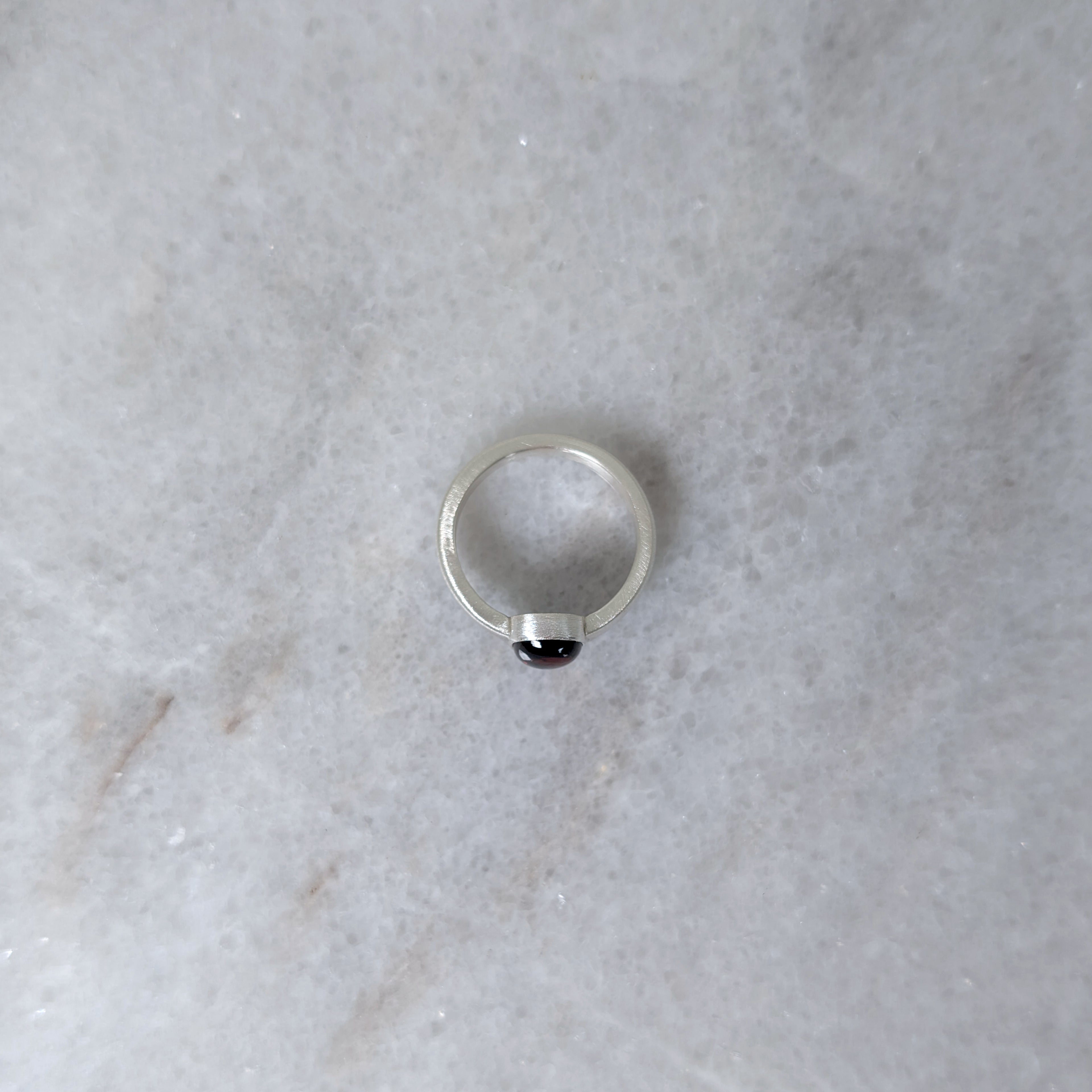 Side view of silver ring with a garnet center stone on a white marble surface
