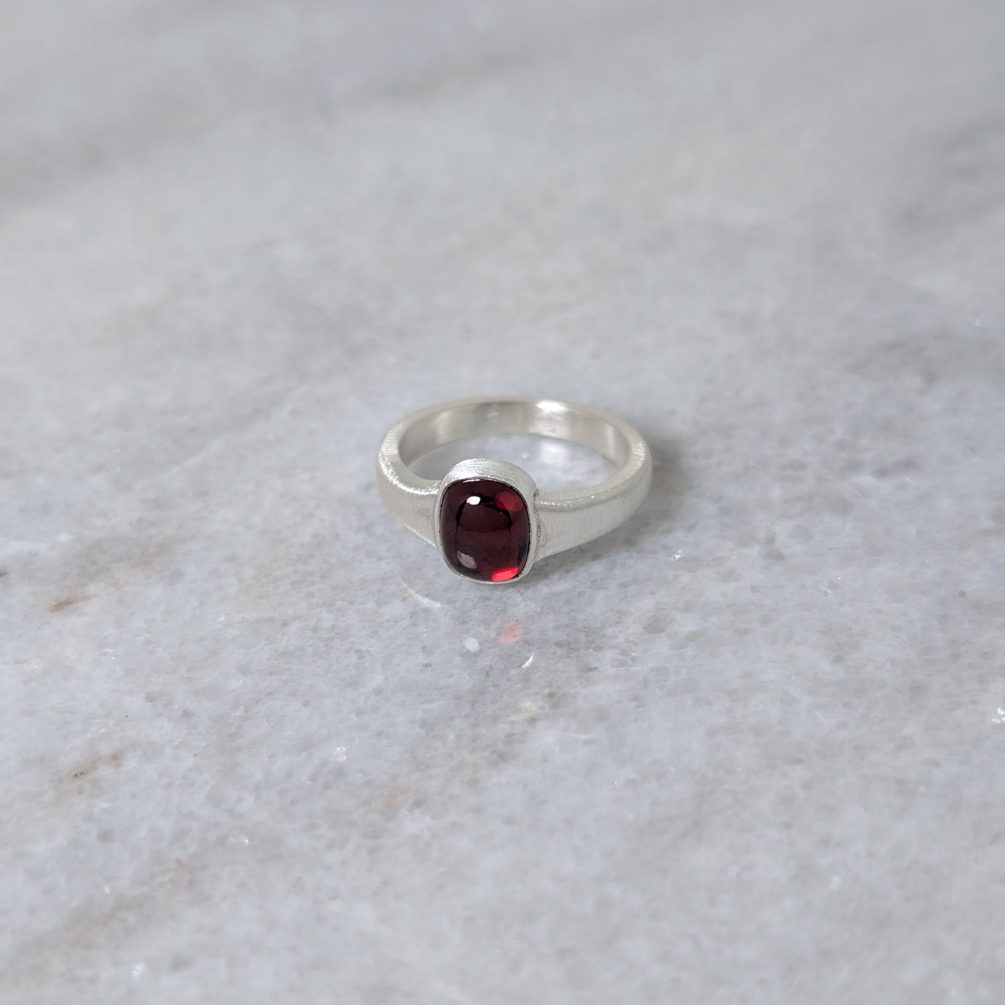 Angled view of silver ring with a garnet center stone on a white marble surface