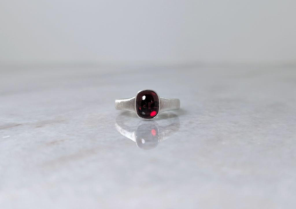 Silver ring with a garnet center stone on a white marble surface
