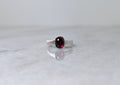 Silver ring with a garnet center stone on a white marble surface