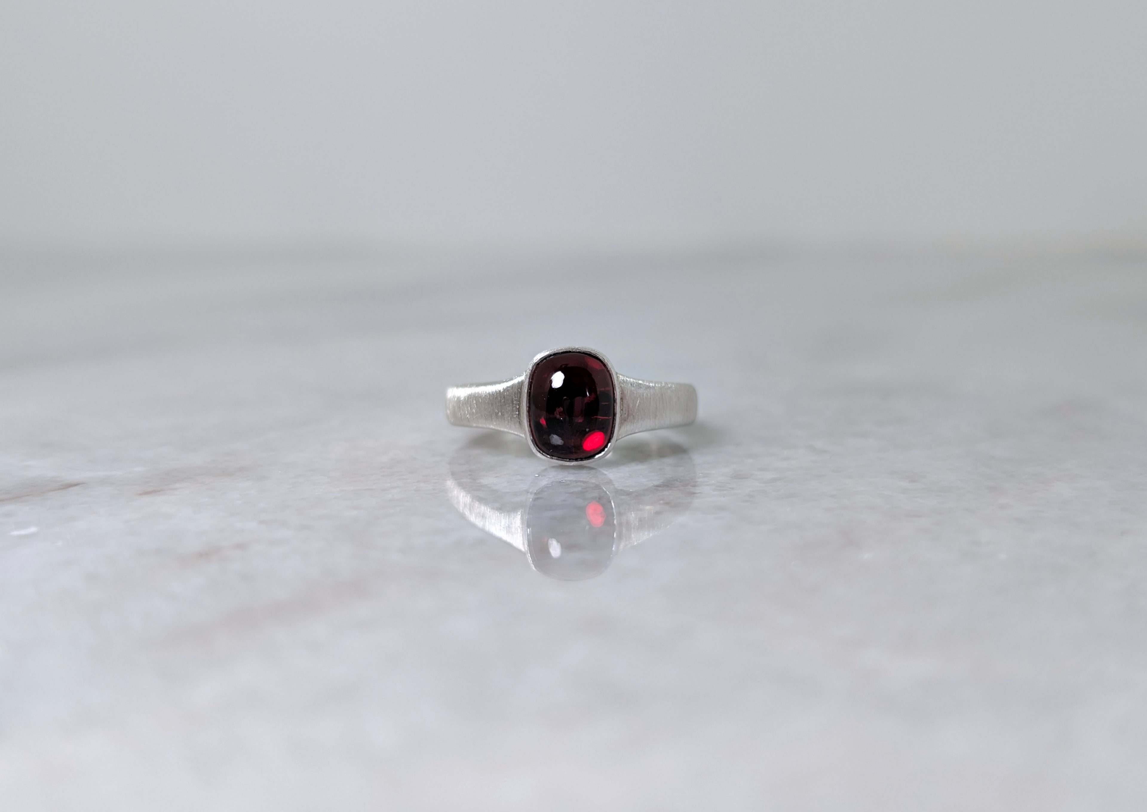 Silver ring with a garnet center stone on a white marble surface