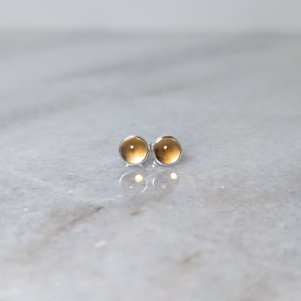 A pair of round citrine cabochons set in silver studs on a marble surface
