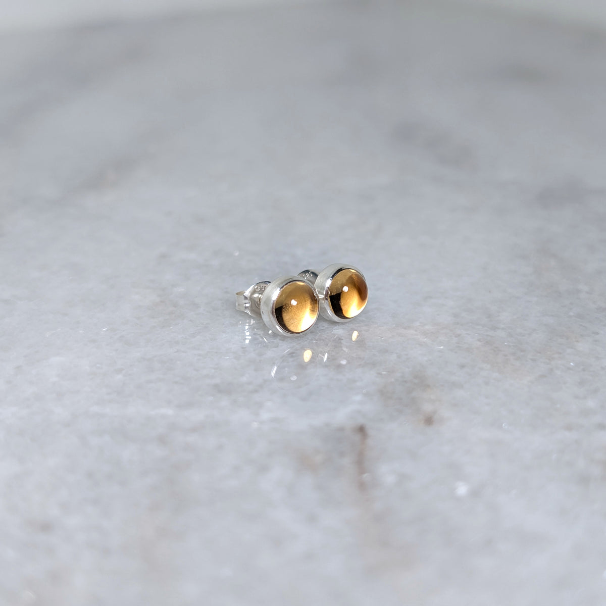 A pair of round citrine cabochons set in silver studs on a marble surface