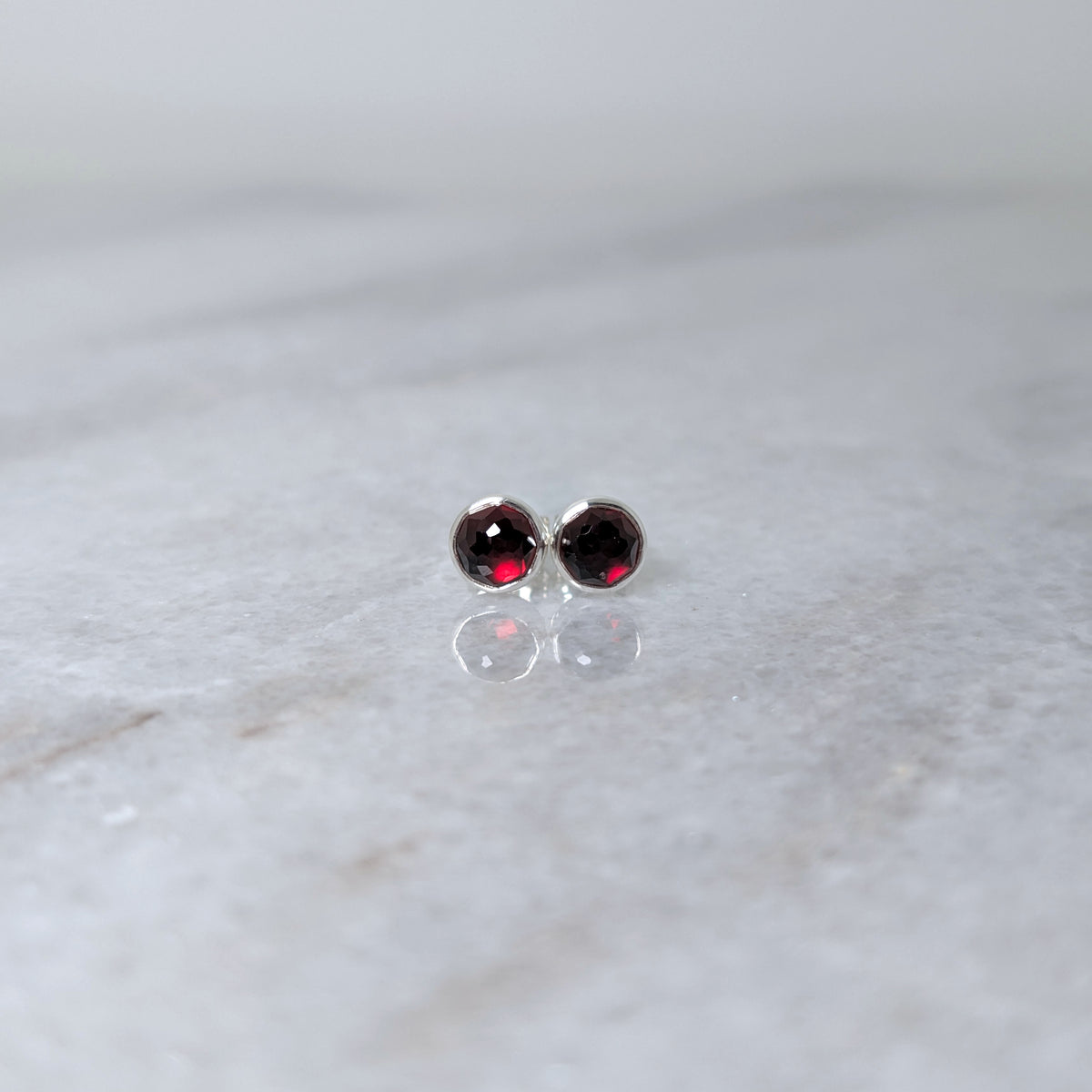 A pair of round garnet rose cut cabochons set in silver studs on a marble surface