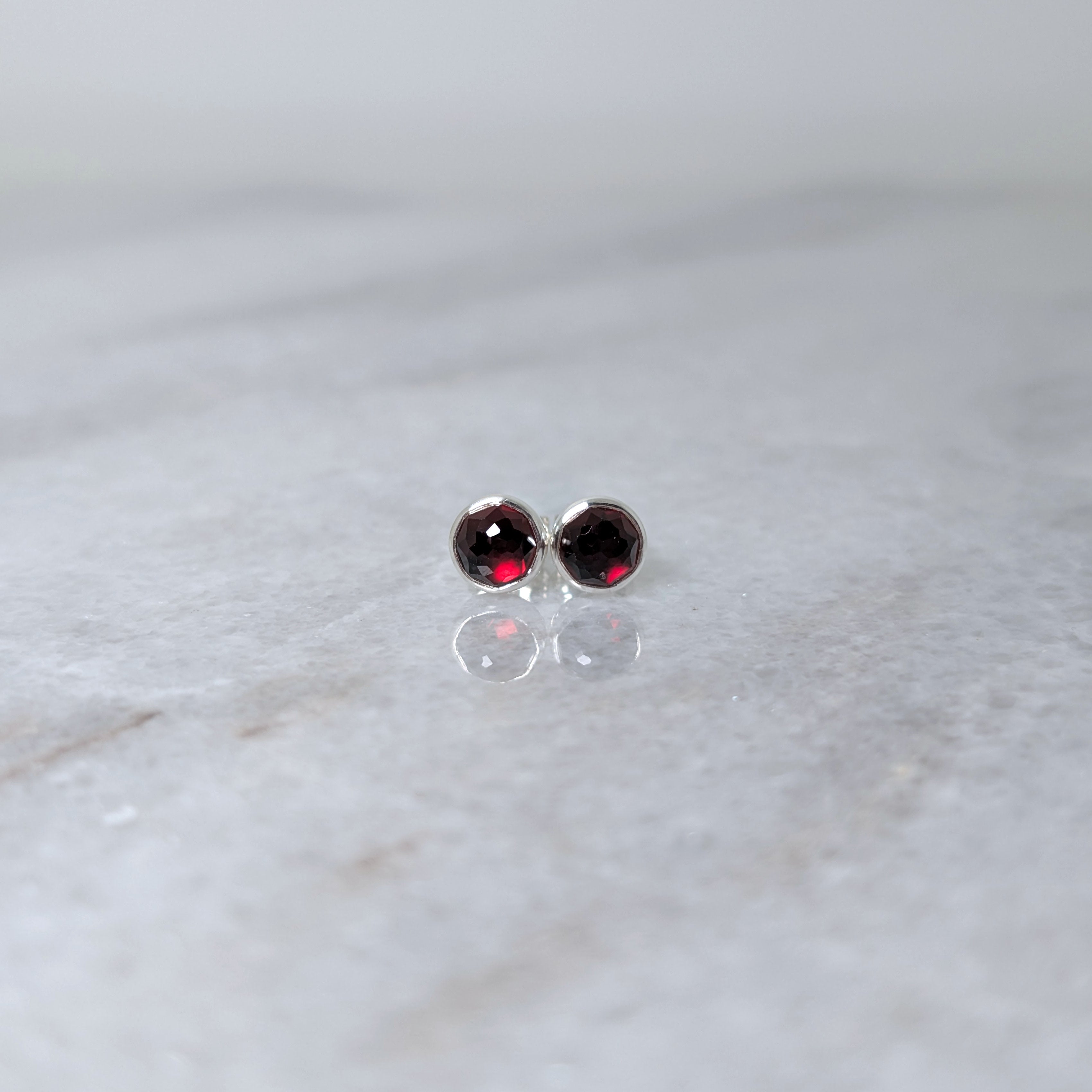 A pair of round garnet rose cut cabochons set in silver studs on a marble surface