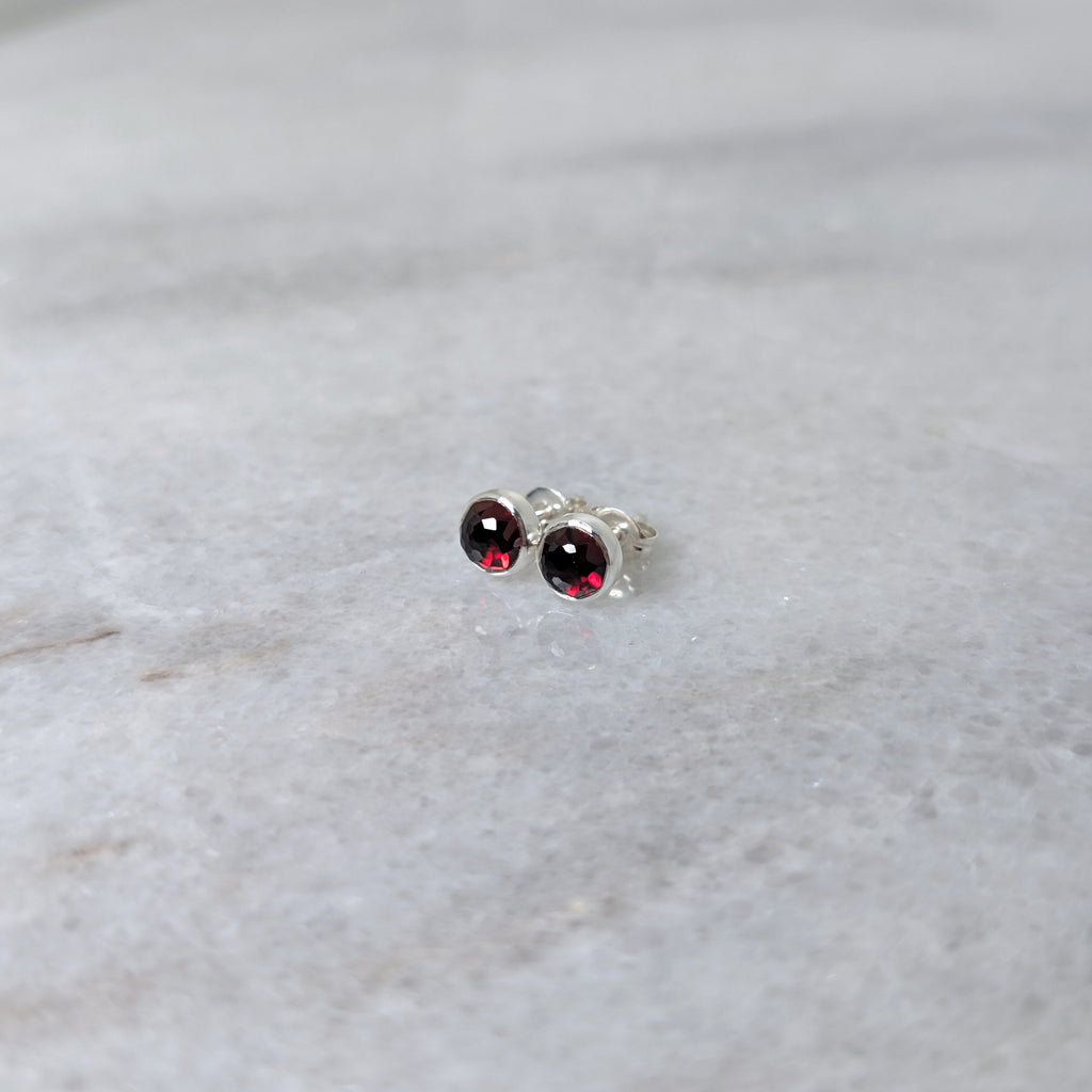 A pair of round garnet rose cut cabochons set in silver studs on a marble surface