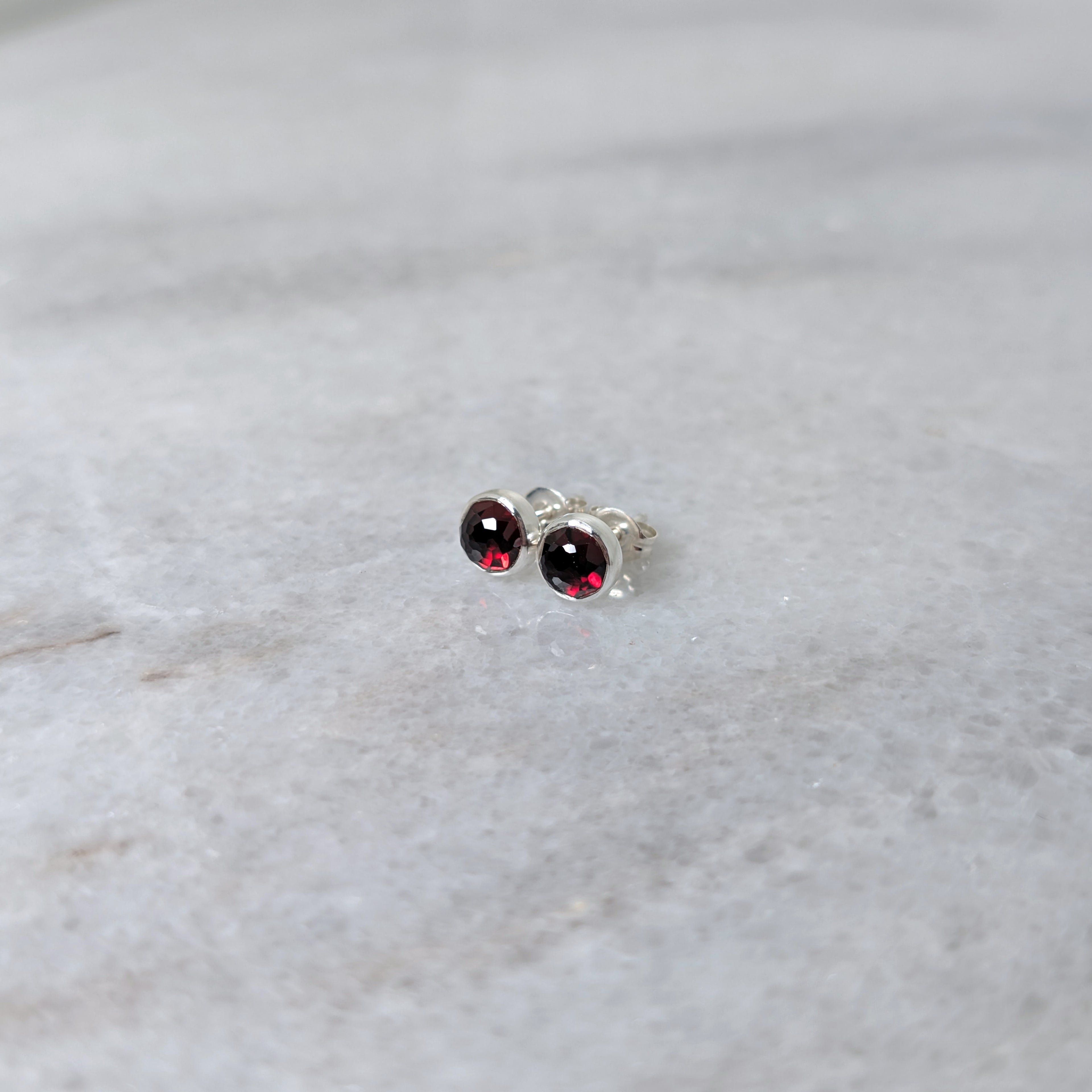 A pair of round garnet rose cut cabochons set in silver studs on a marble surface