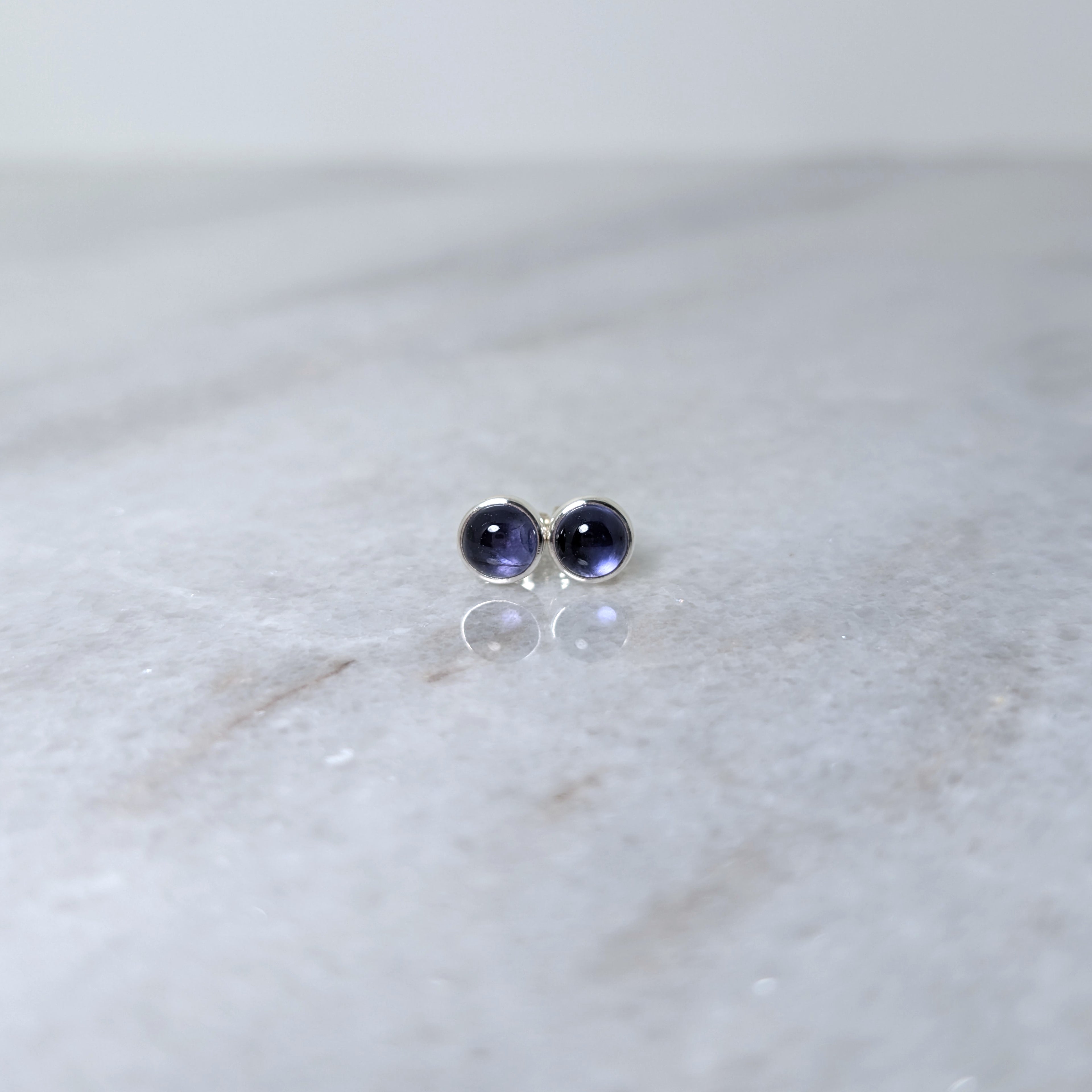 A pair of round iolite cabochons set in silver studs on a marble surface