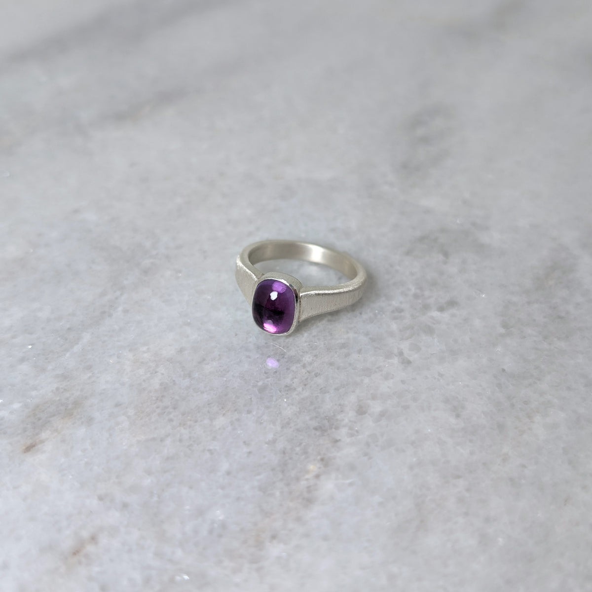 Silver ring with an amethyst center stone on a white marble background