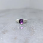 Silver ring with an amethyst center stone on a white marble background