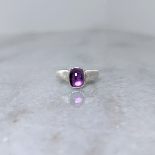 Silver ring with an amethyst center stone on a white marble background