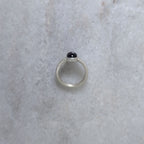 Side view of a silver ring with an amethyst center stone on a white marble background
