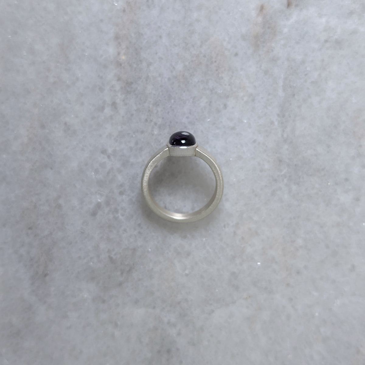 Side view of a silver ring with an amethyst center stone on a white marble background