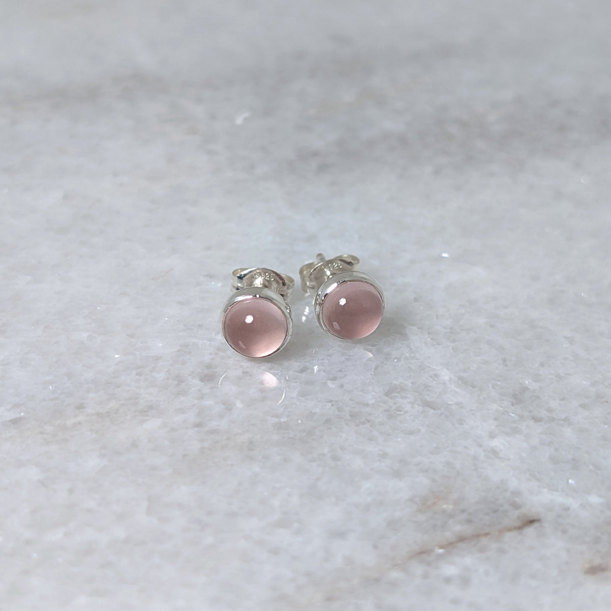 A pair of round rose quartz cabochons set in silver studs on a marble surface