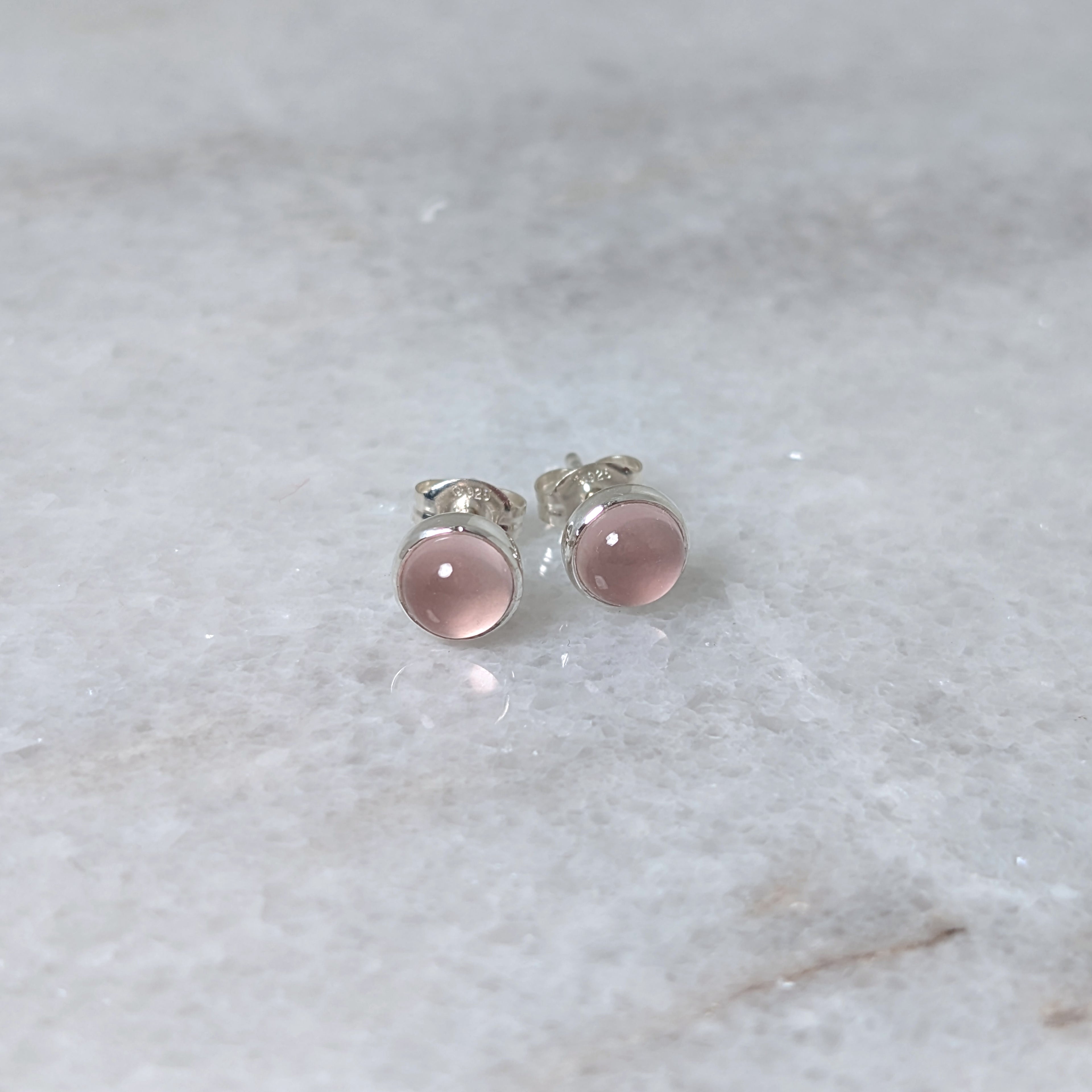 A pair of round rose quartz cabochons set in silver studs on a marble surface