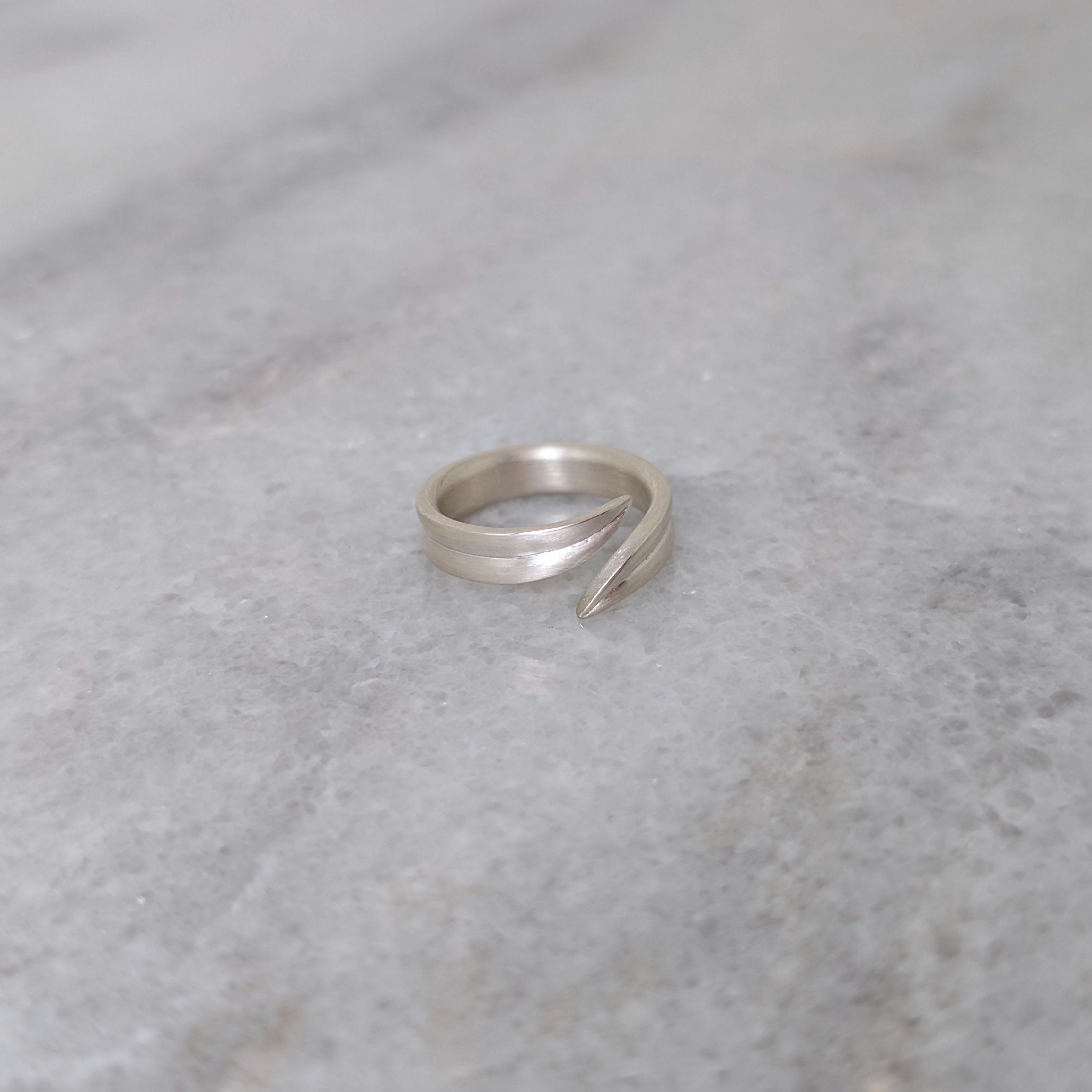 Angled view of a silver leaf blade ring on a marble surface