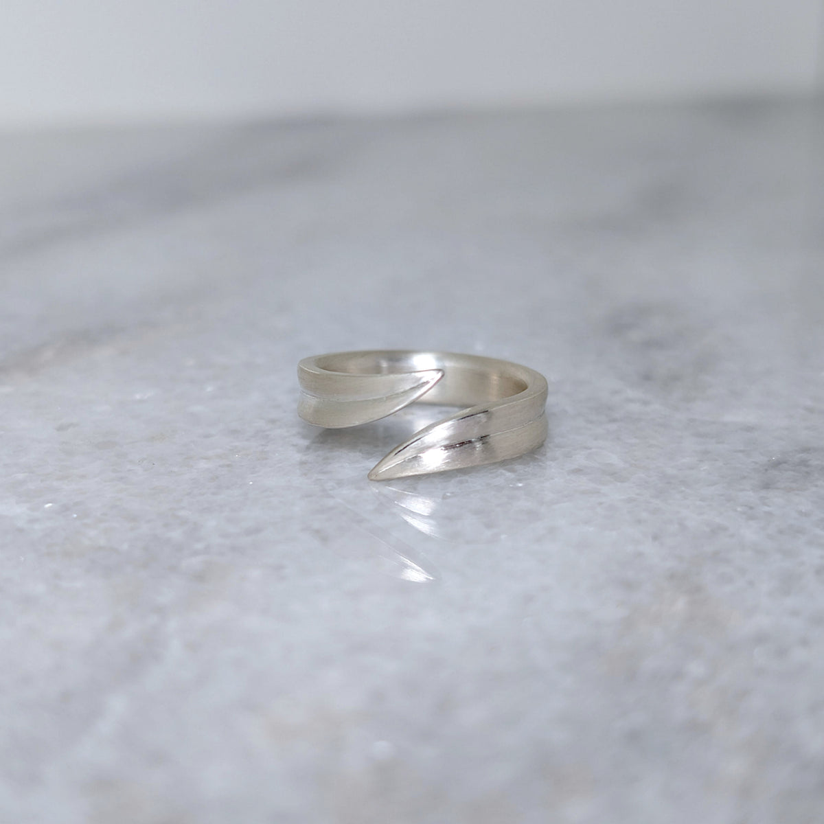 Silver leaf blade ring with an open top on a marble surface