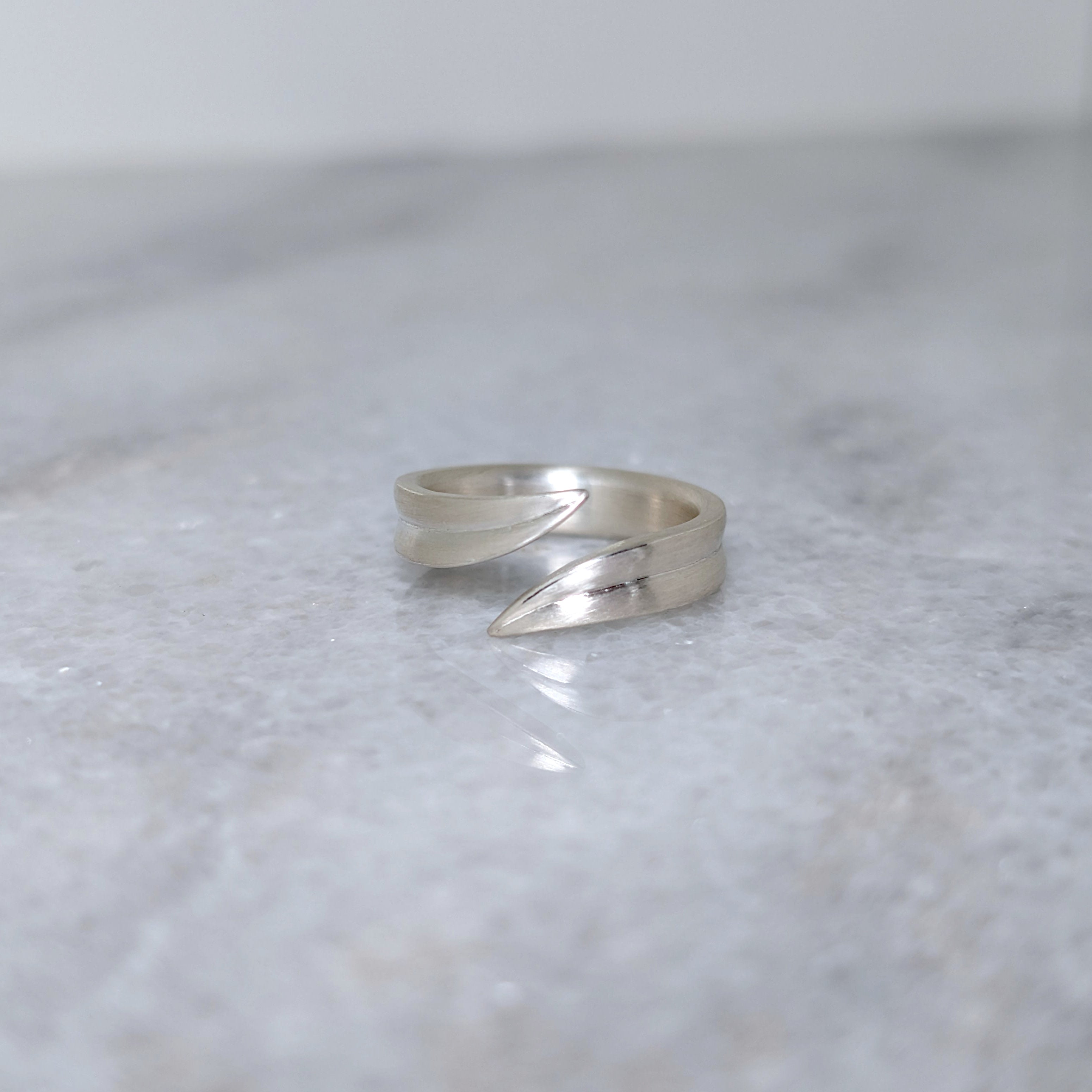 Silver leaf blade ring with an open top on a marble surface