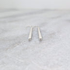 Faceted end detail of Silver tapered bar earrings on a white marble surface