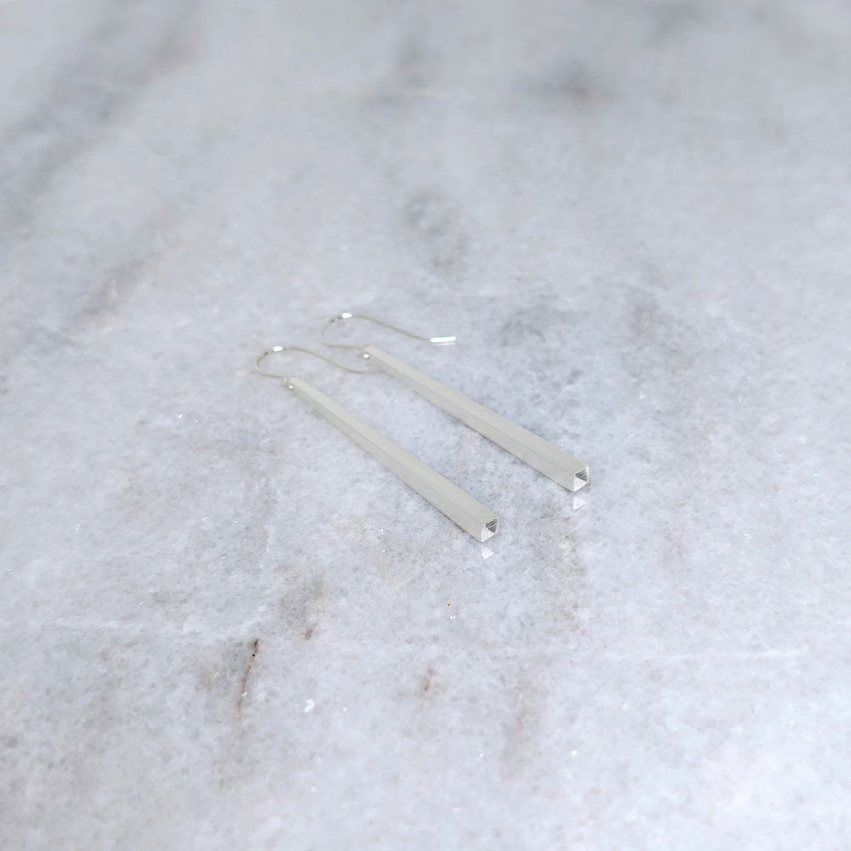 Silver tapered earrings on a marble surface