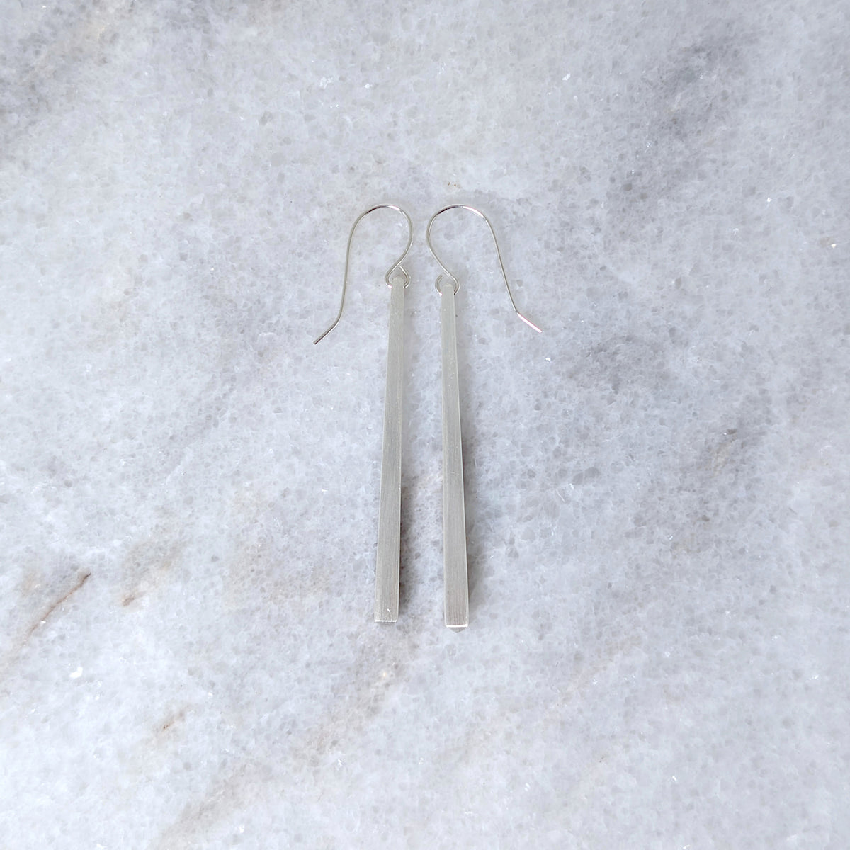 Silver tapered bar earrings on a white marble surface