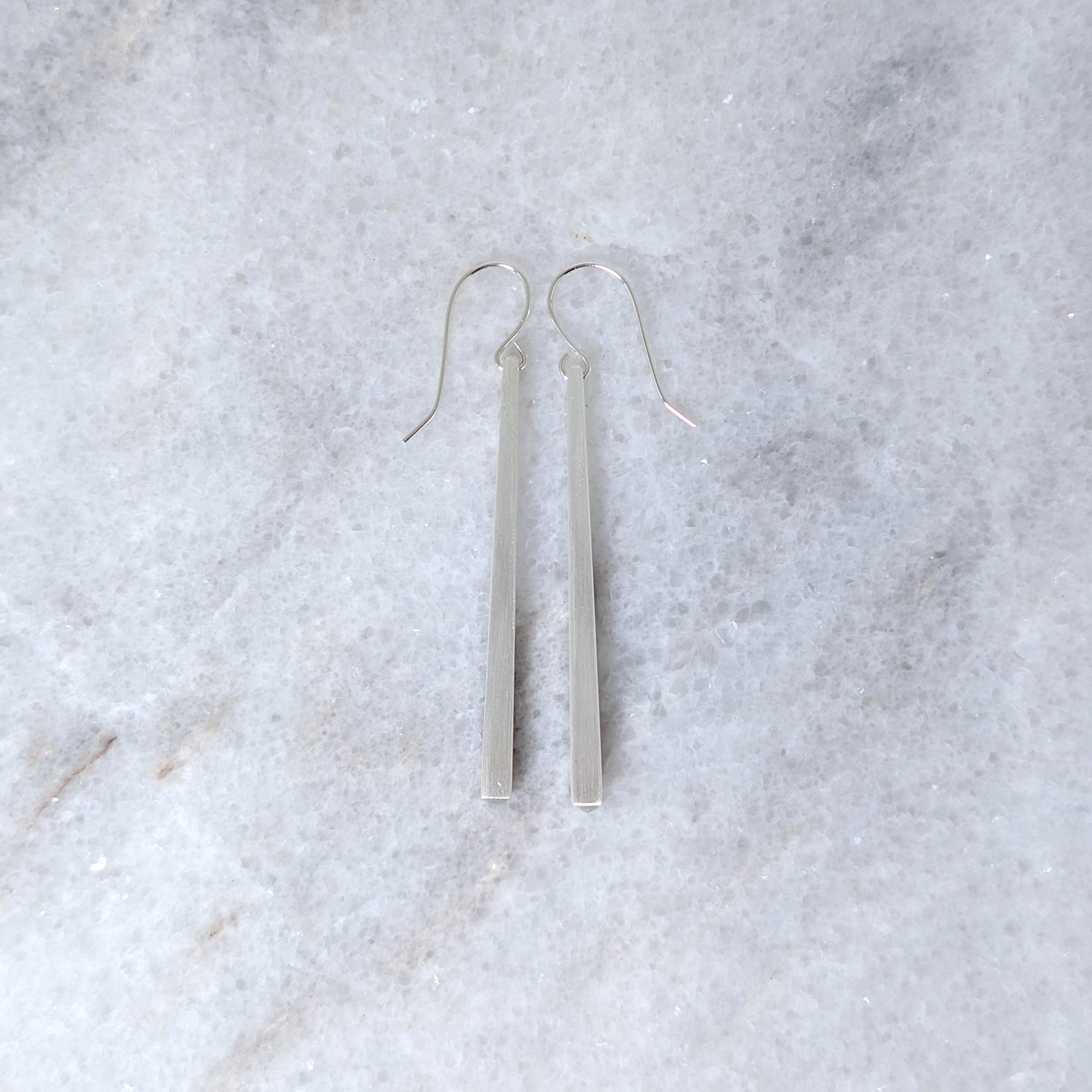 Silver tapered bar earrings on a white marble surface