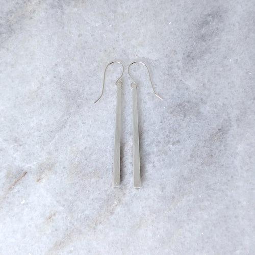 Silver tapered bar earrings on a white marble surface